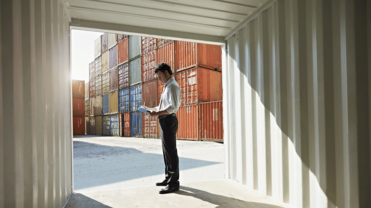 View looking out of empty container at shipping dock with man looking at paperwork in his hands